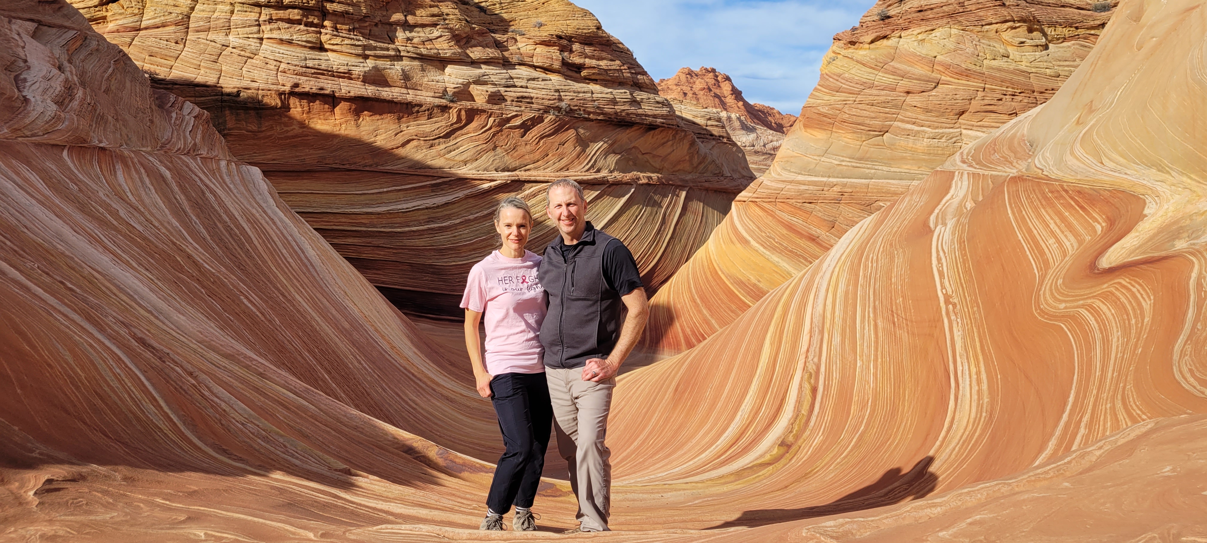 A man and a woman pose together in a vibrant, colorful sandstone landscape featuring swirling patterns in The Wave, located in Arizona.